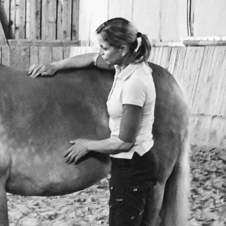 Woman standing beside the back of a horse applying equine acupressure (c) IF Equine Therapies