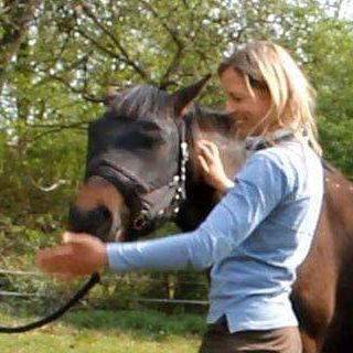 Woman and horse. Woman standing beside horse's head having her right hand at the top of the neck and her left in front of the muzzle which the horse is sniffing at (c) IF Equine Therapies